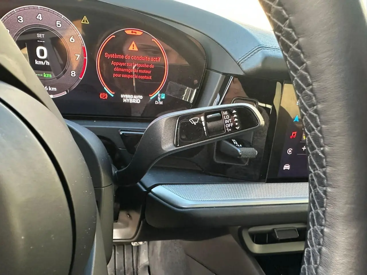 Vue rapprochée du tableau de bord et du volant d’un Porsche Cayenne hybride 2024 avec affichage numérique et commandes au volant.