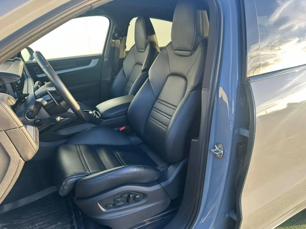 Vue intérieure côté conducteur du Porsche Cayenne 2024 gris arctique, mettant en valeur les sièges en cuir noir et le tableau de bord.