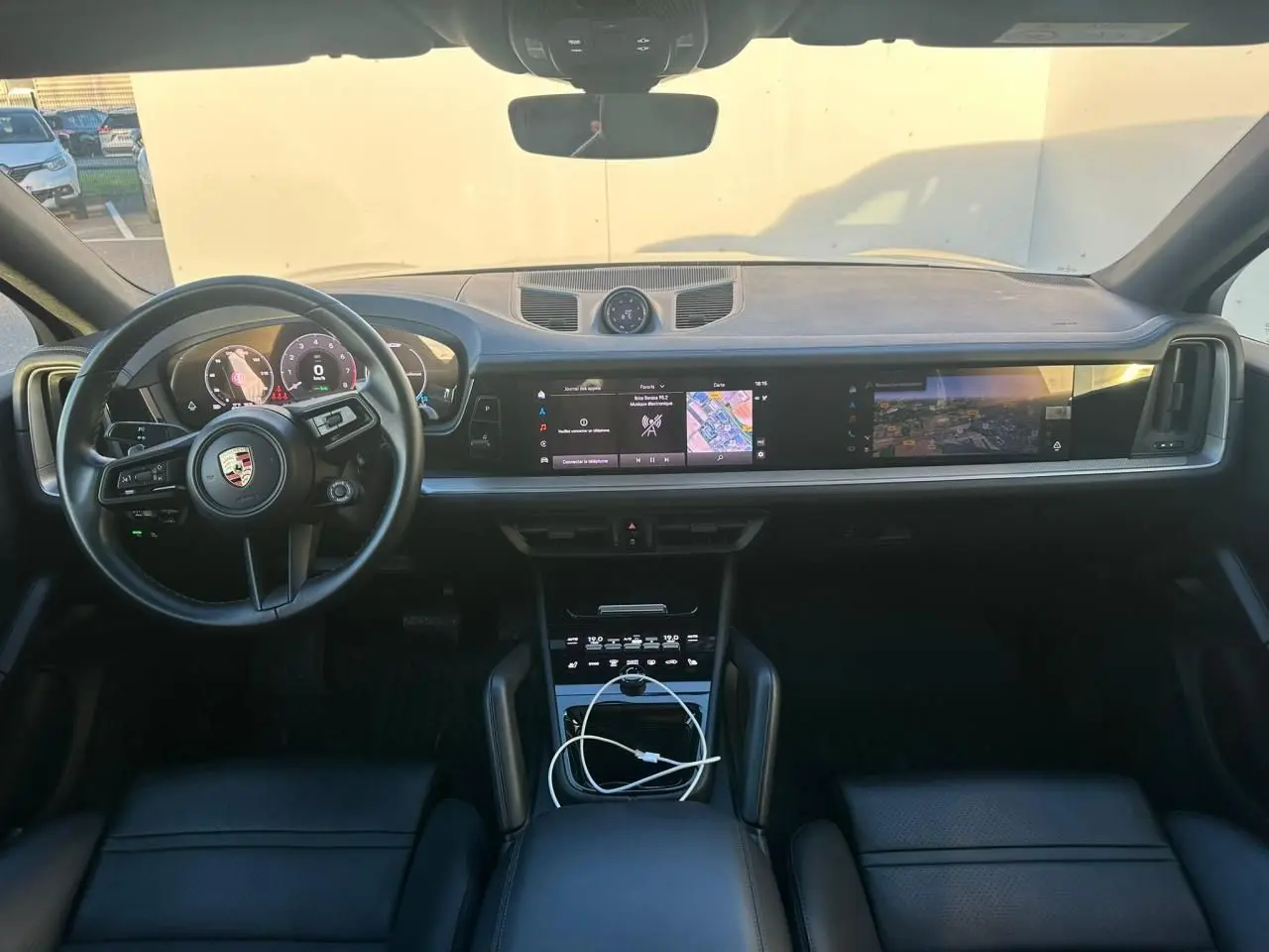 Vue intérieure frontale du tableau de bord du Porsche Cayenne 2024, avec écran tactile panoramique et volant multifonction noir.
