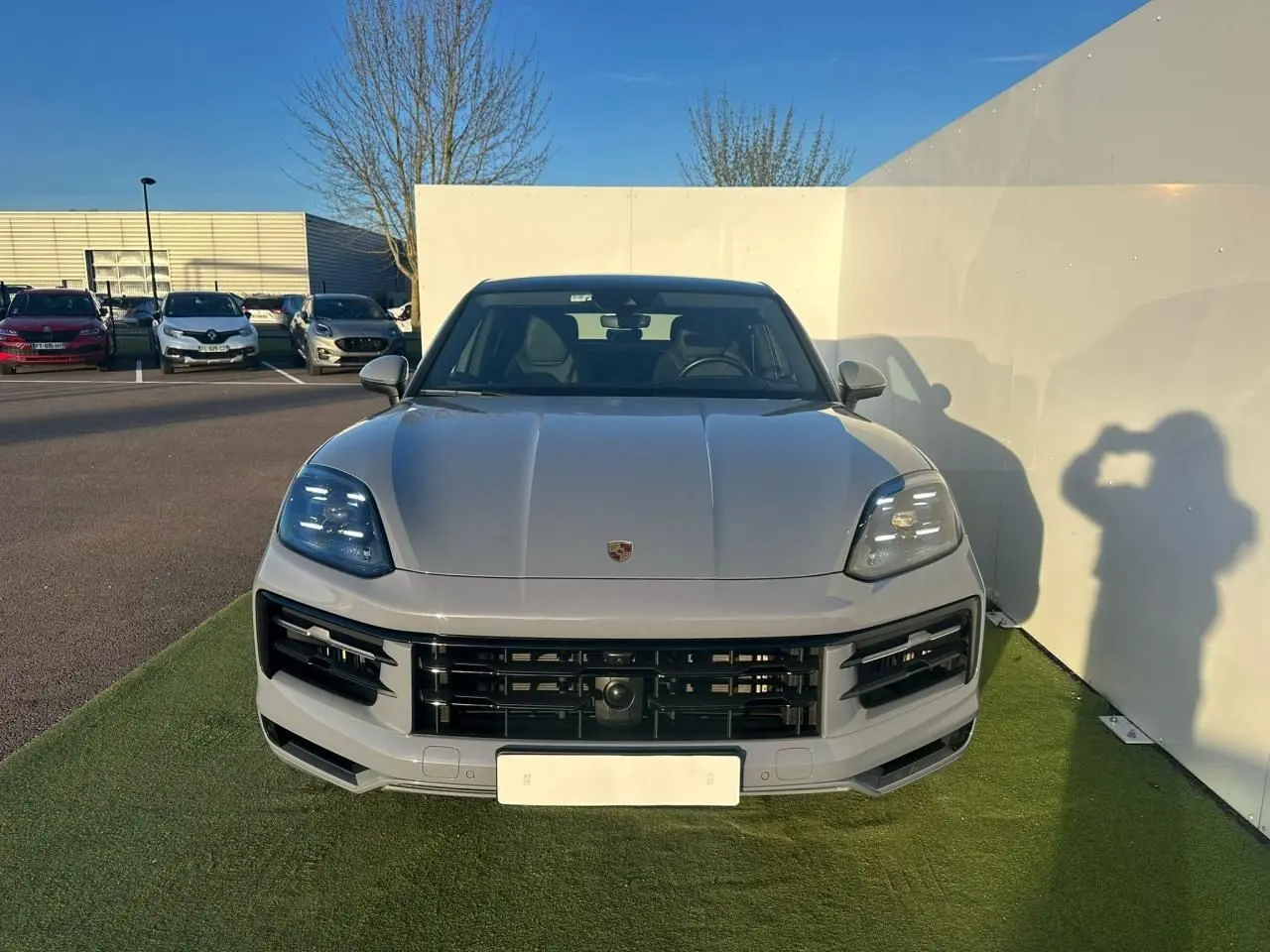 Vue avant d'un Porsche Cayenne III Coupe 3.0 V6 S E-Hybrid 2024 en gris arctique, avec calandre noire et phares LED.