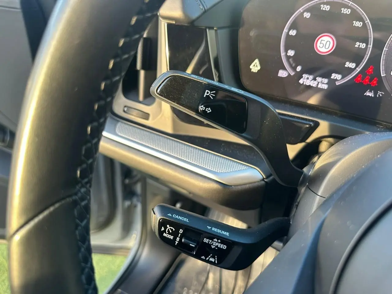 Gros plan sur les commandes au volant du Porsche Cayenne gris arctique, avec tableau de bord numérique en arrière-plan.