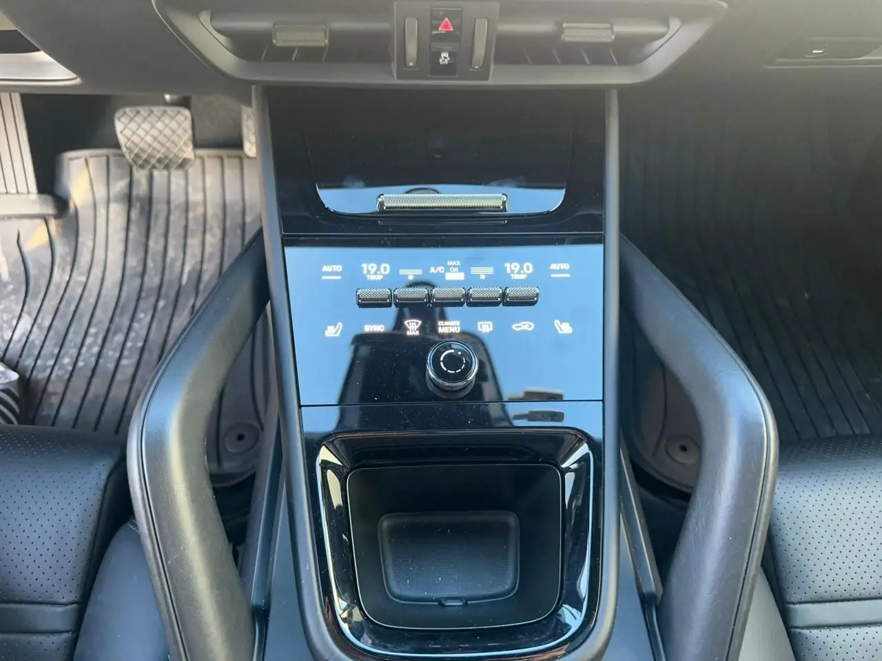 Vue rapprochée de la console centrale noire brillante du Porsche Cayenne 2024 avec commandes climatisation et espace de rangement.