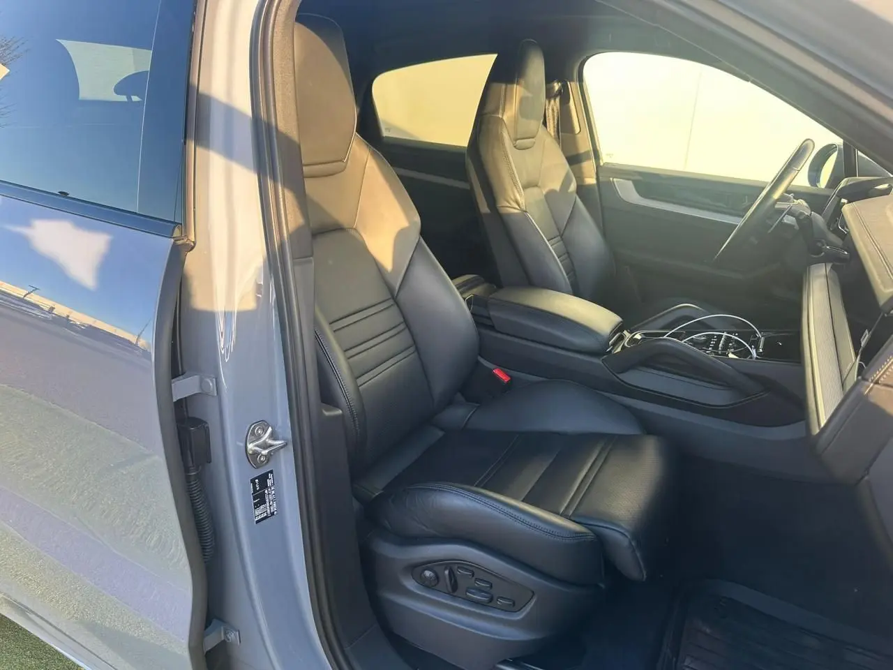 Vue intérieure côté conducteur du Porsche Cayenne 2024 gris arctique, mettant en valeur les sièges en cuir noir et la console centrale.