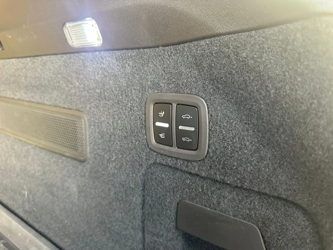 Boutons de réglage des sièges et ouverture du coffre sur la garniture intérieure grise du coffre d’un Porsche Cayenne 2024.