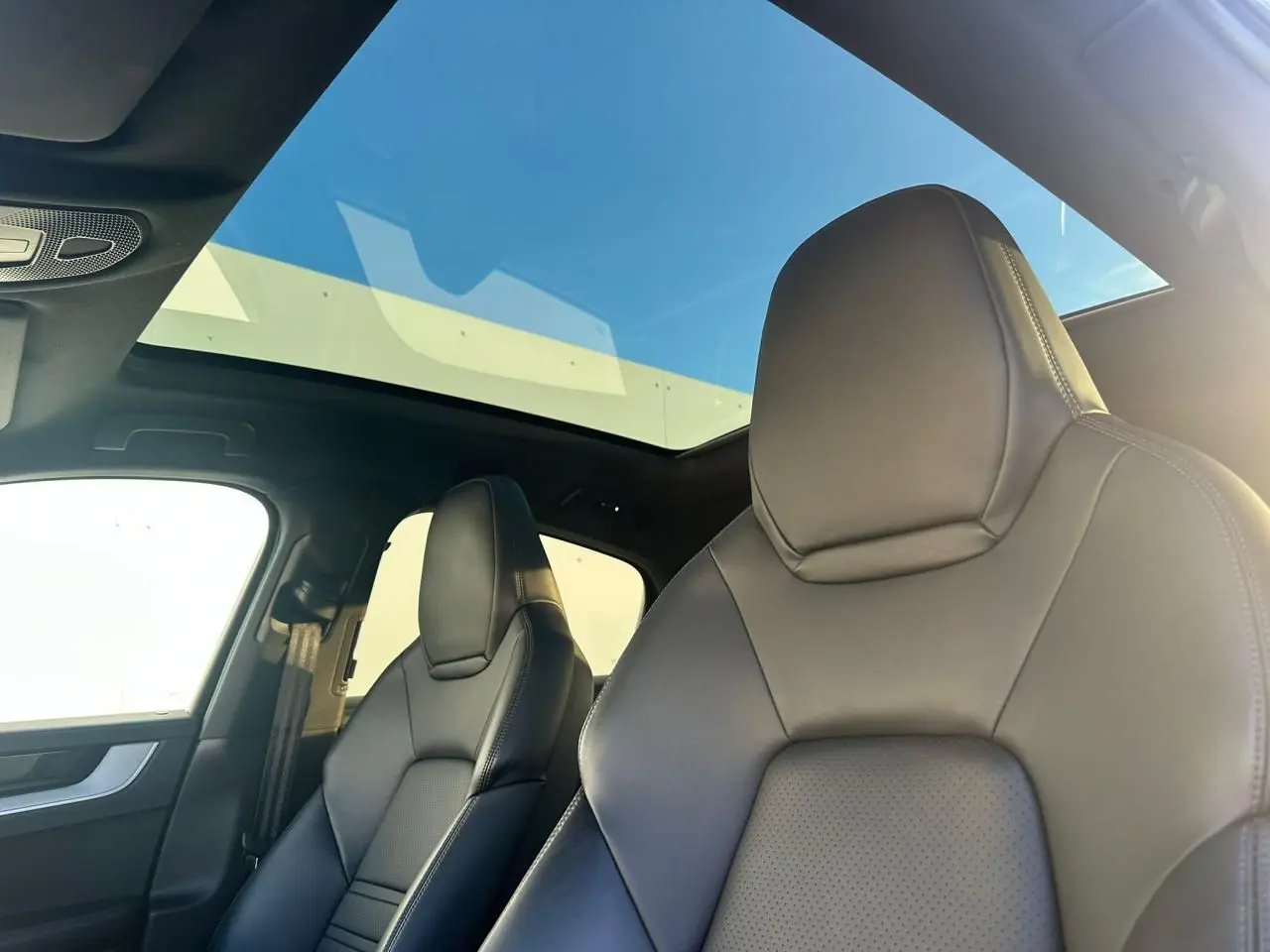 Vue intérieure sur les sièges avant en cuir noir du Porsche Cayenne 2024 avec toit panoramique et lumière naturelle.