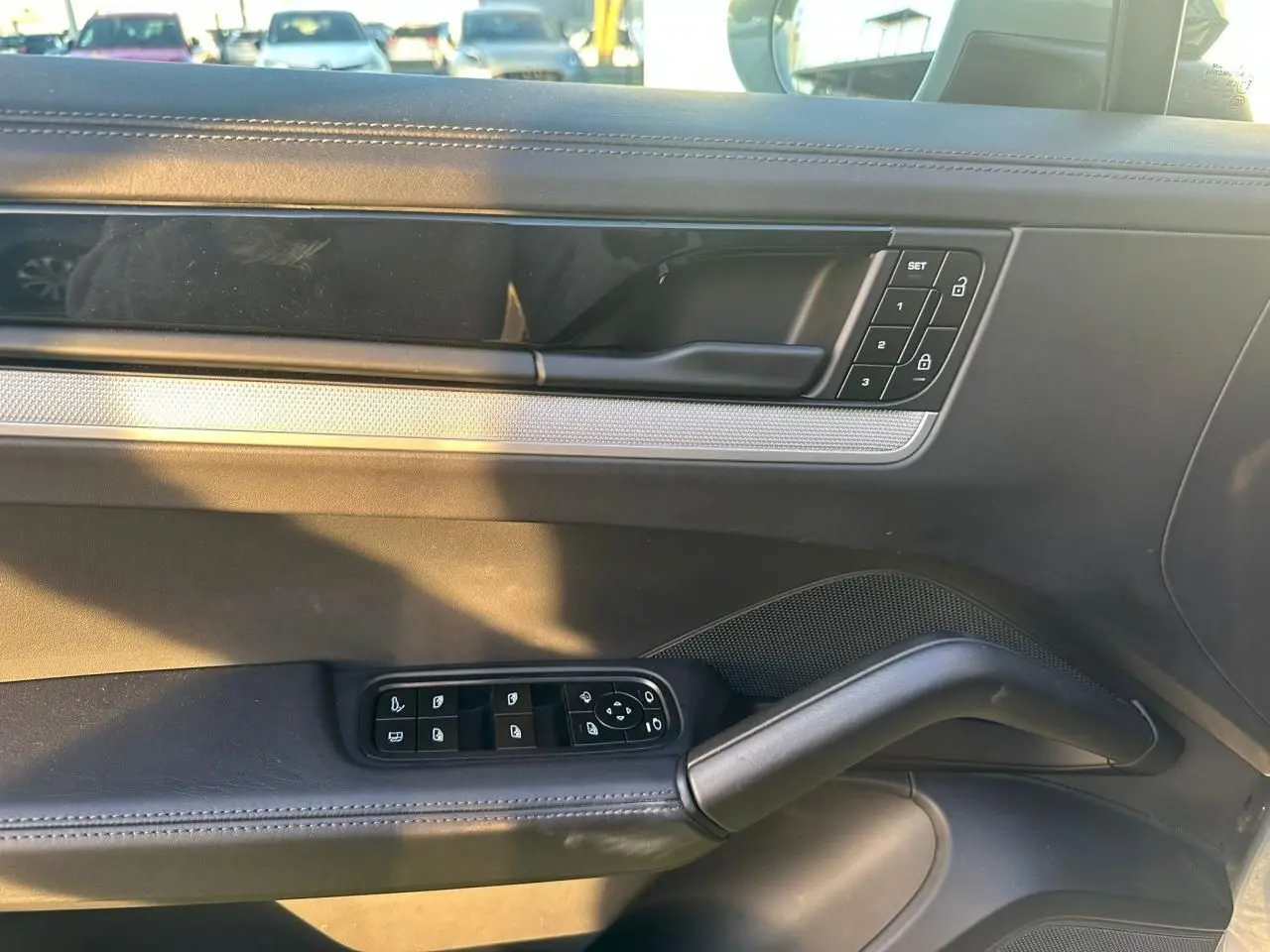 Vue intérieure côté gauche de la porte d’une Porsche Cayenne 2024 gris arctique, avec commandes de vitres et verrouillage.