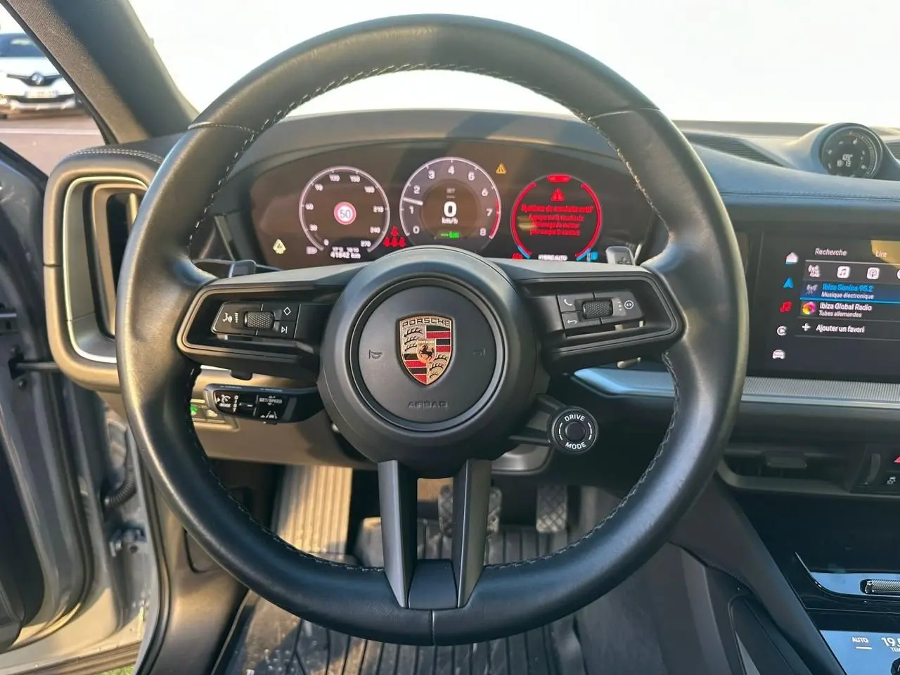 Vue intérieure centrée sur le volant noir du Porsche Cayenne 2024 avec tableau de bord numérique et écran tactile.