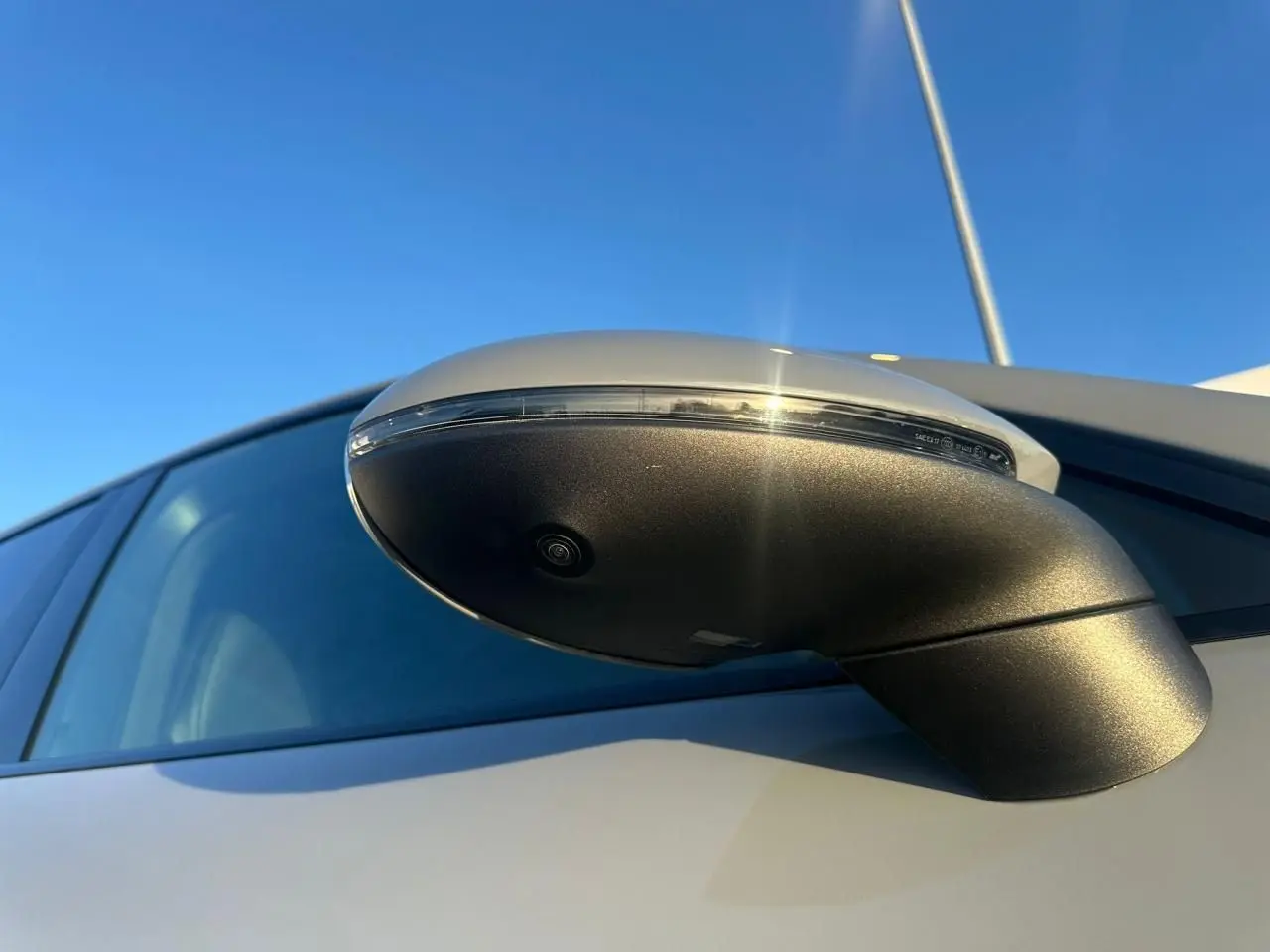Gros plan sur le rétroviseur côté droit gris arctique du Porsche Cayenne III Coupe 2024, avec caméra intégrée visible.