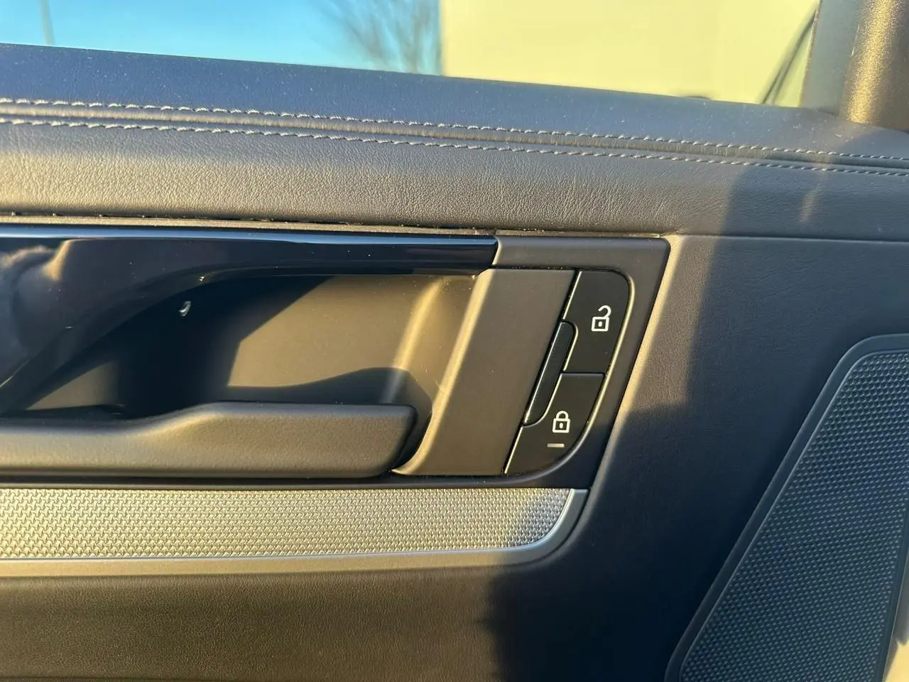 Détail de la poignée intérieure côté gauche de la porte d’un Porsche Cayenne 2024 gris arctique, avec commandes de verrouillage.