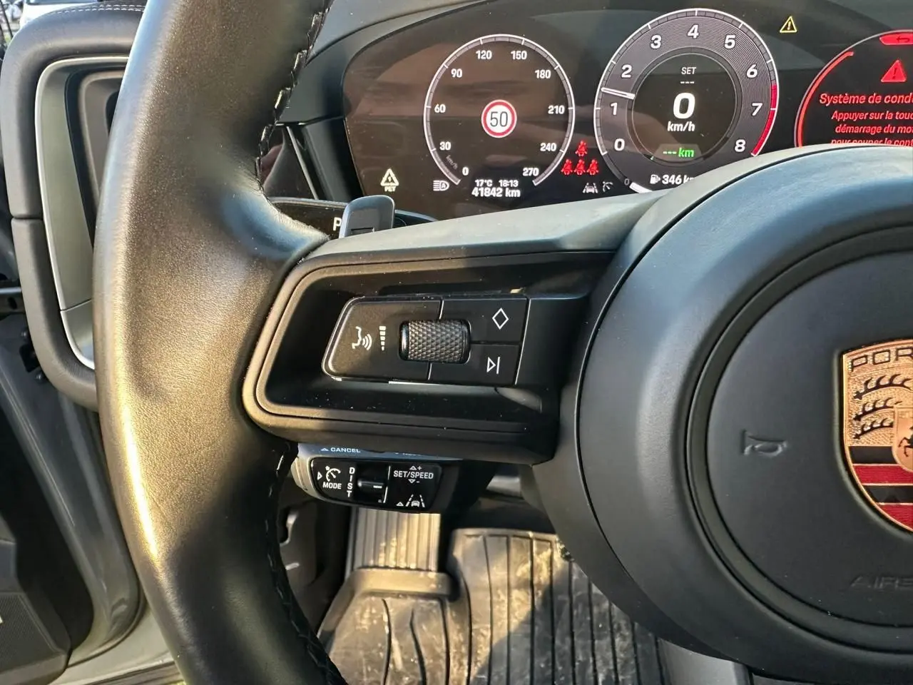 Gros plan sur le volant et le tableau de bord numérique du Porsche Cayenne 2024, avec commandes au volant visibles.