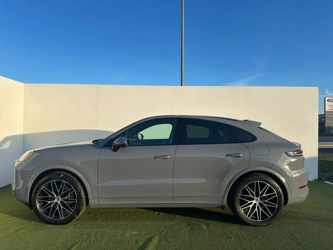 Vue de profil côté gauche d'un Porsche Cayenne Coupé 2024 en gris arctique avec jantes noires à rayons fins.