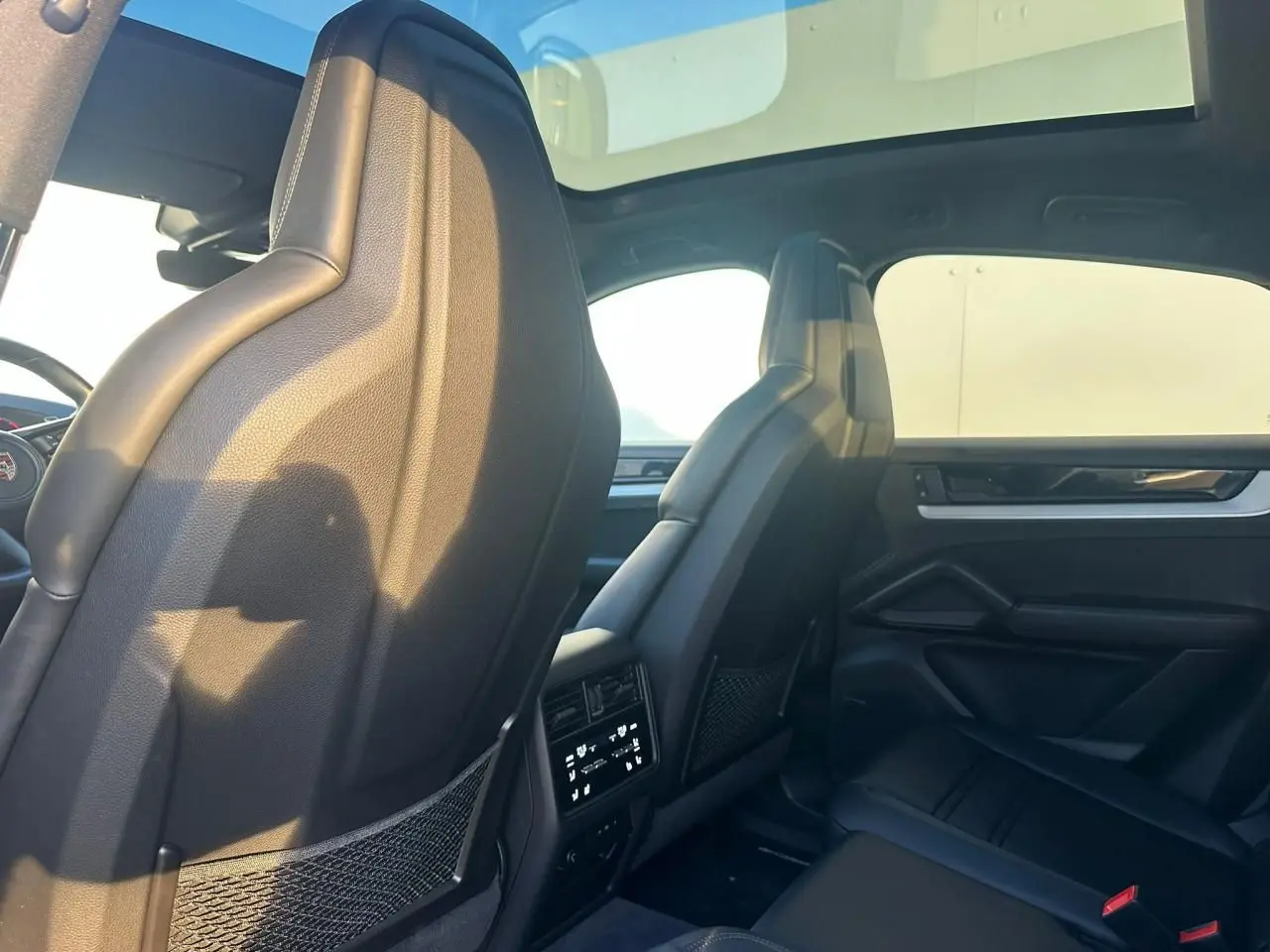 Vue intérieure arrière du Porsche Cayenne 2024 gris arctique, montrant les sièges avant en cuir noir et toit panoramique.
