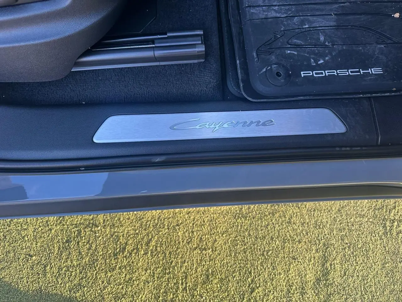 Gros plan sur la plaque de seuil de porte côté conducteur du Porsche Cayenne gris arctique avec tapis de sol Porsche visible.