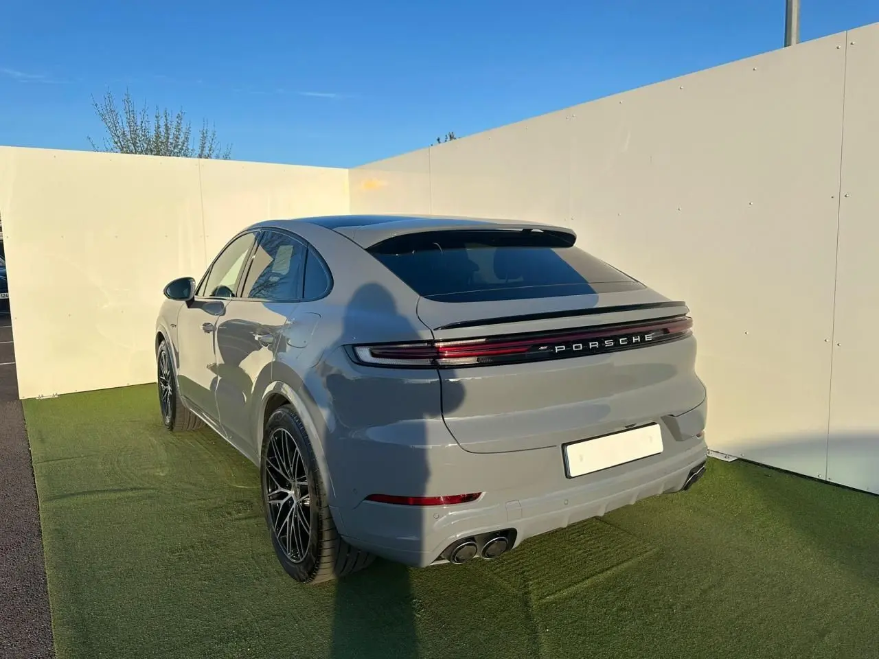 Vue 3/4 arrière droite d'un Porsche Cayenne Coupé 2024 gris arctique avec feux arrière continus et double sortie d'échappement.