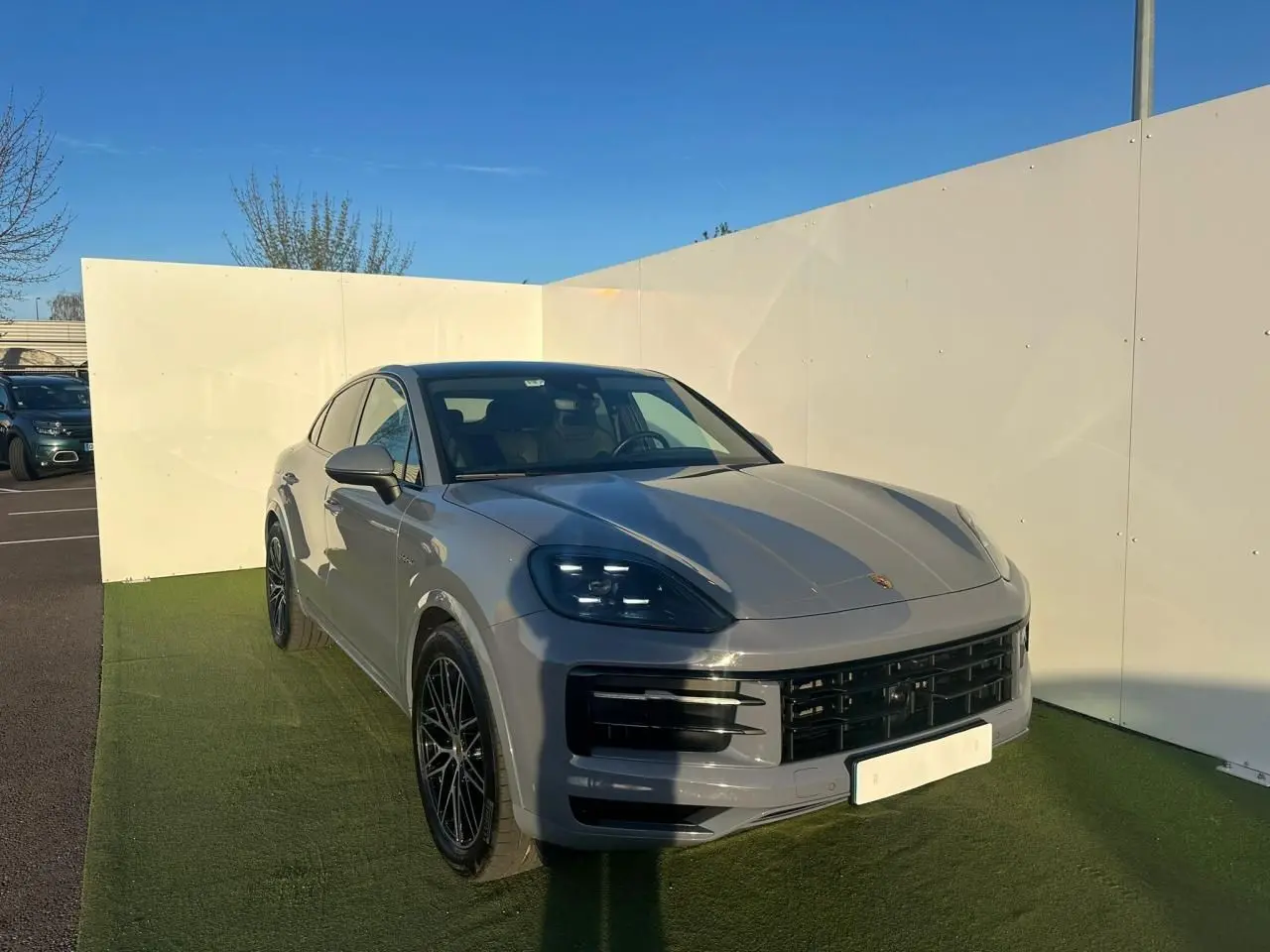 Vue 3/4 avant droite du Porsche Cayenne III Coupe 3.0 V6 S E-Hybrid 2024 en gris arctique avec jantes noires.