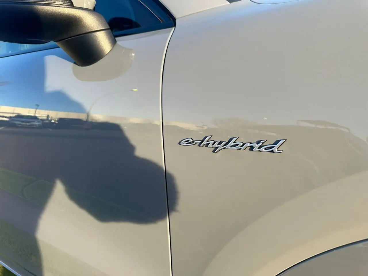 Gros plan sur l’inscription e-hybrid côté gauche d’un Porsche Cayenne Coupé gris arctique 2024, avec rétroviseur noir.