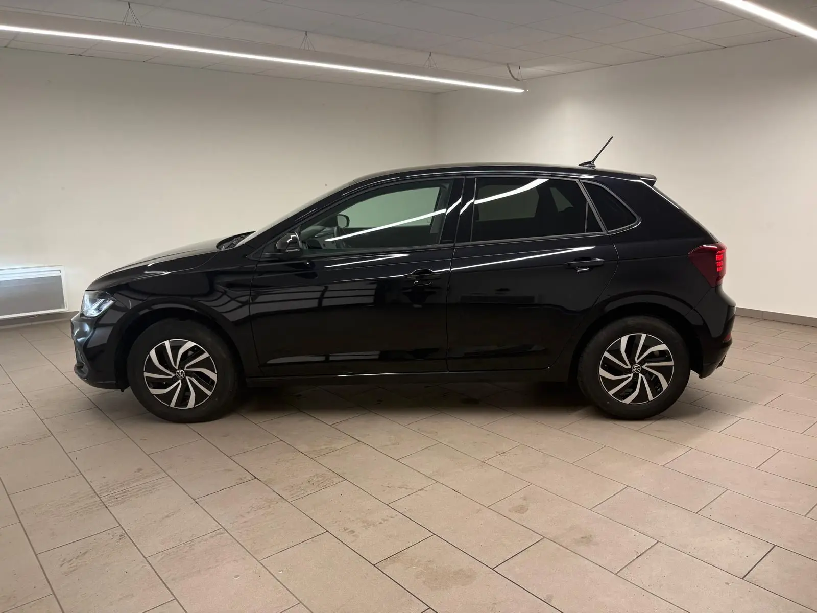 Vue de profil côté gauche d'une Volkswagen Polo noire intense 2025 dans un intérieur neutre, avec jantes alliage 15 pouces.