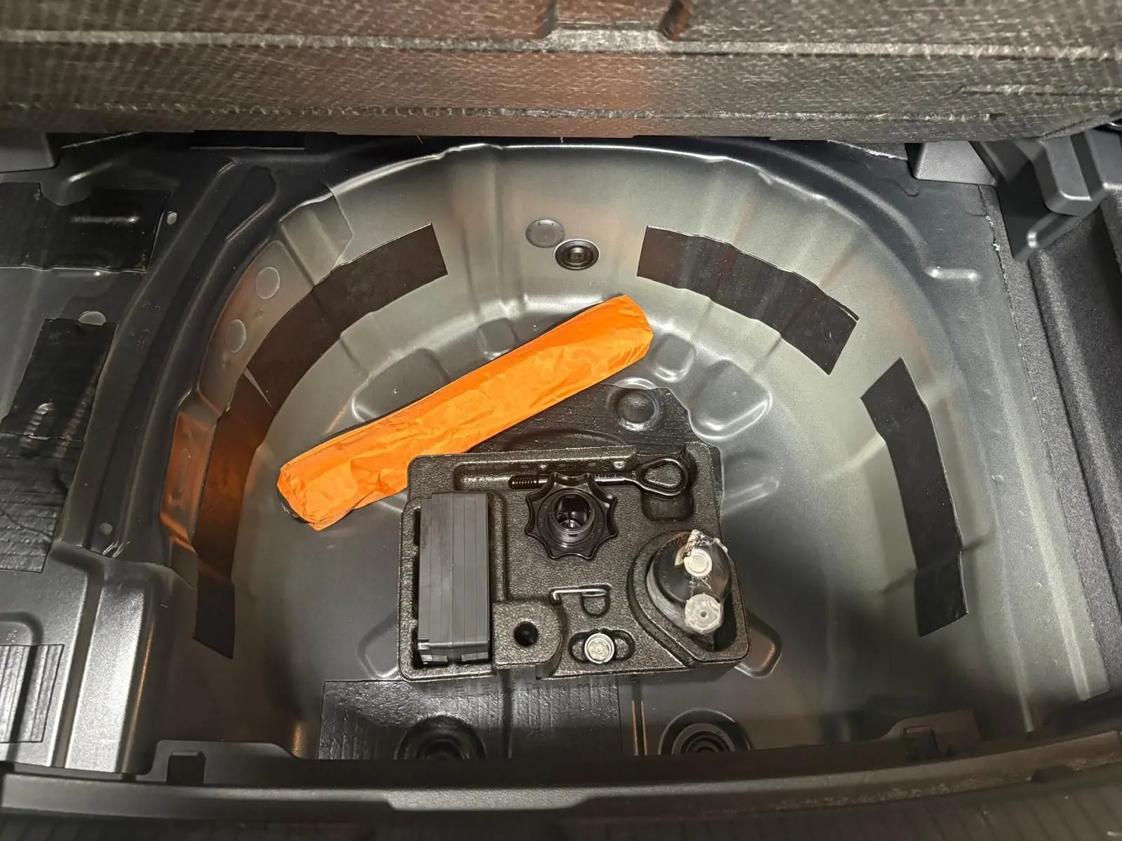 Vue plongeante sur le coffre ouvert de la Volkswagen Polo noir intense, montrant le rangement sous plancher avec kit de dépannage.