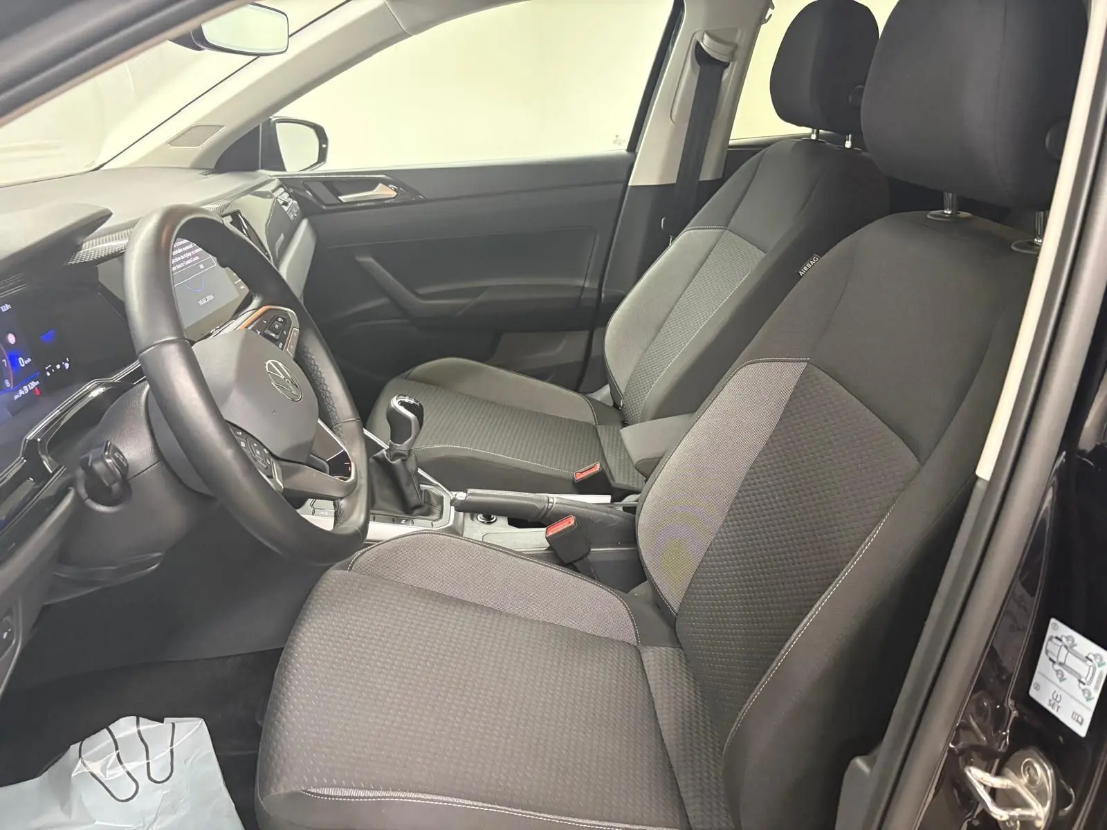 Vue intérieure côté conducteur de la Volkswagen Polo 2025, sièges tissu gris et volant cuir avec levier de vitesses manuel.