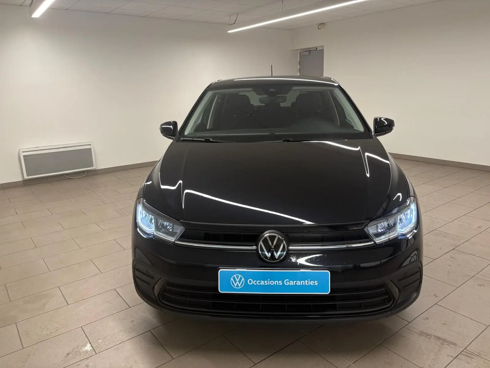 Vue frontale d'une Volkswagen Polo noire intense avec phares LED allumés dans un showroom.