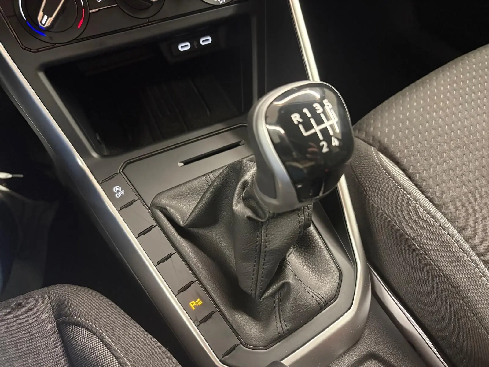 Gros plan sur levier de vitesses manuel noir et console centrale avec sièges tissu gris dans Volkswagen Polo 2025.