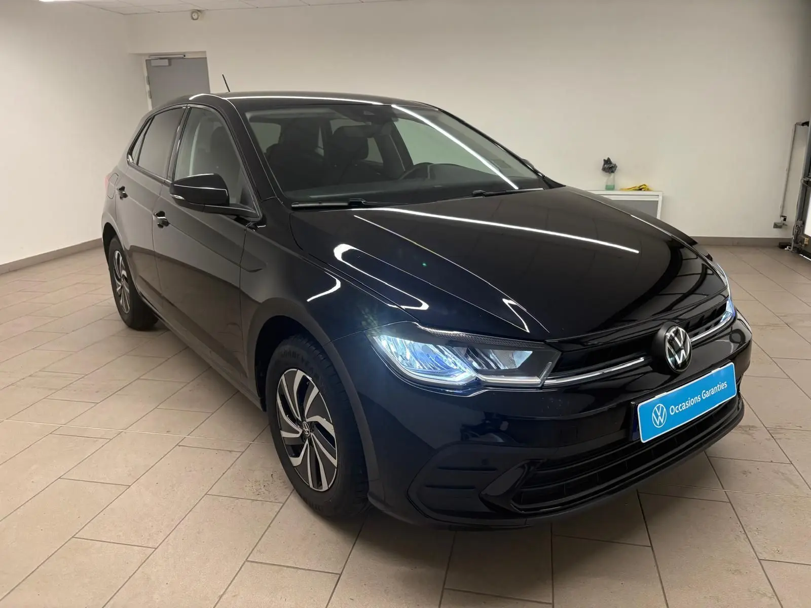 Volkswagen Polo noir intense vue 3/4 avant droit avec phares LED allumés en intérieur showroom.