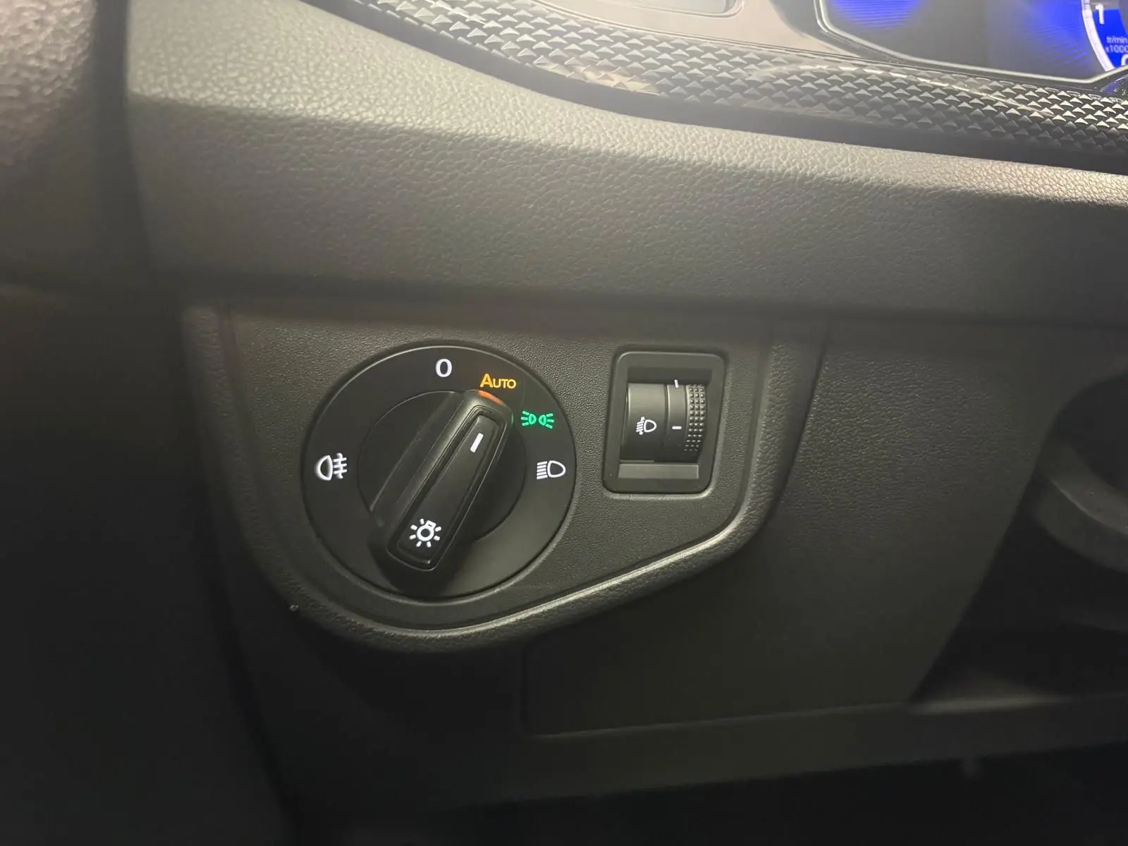 Gros plan sur le bouton d'allumage automatique des phares avec réglage d'intensité sur tableau de bord noir de Volkswagen Polo.