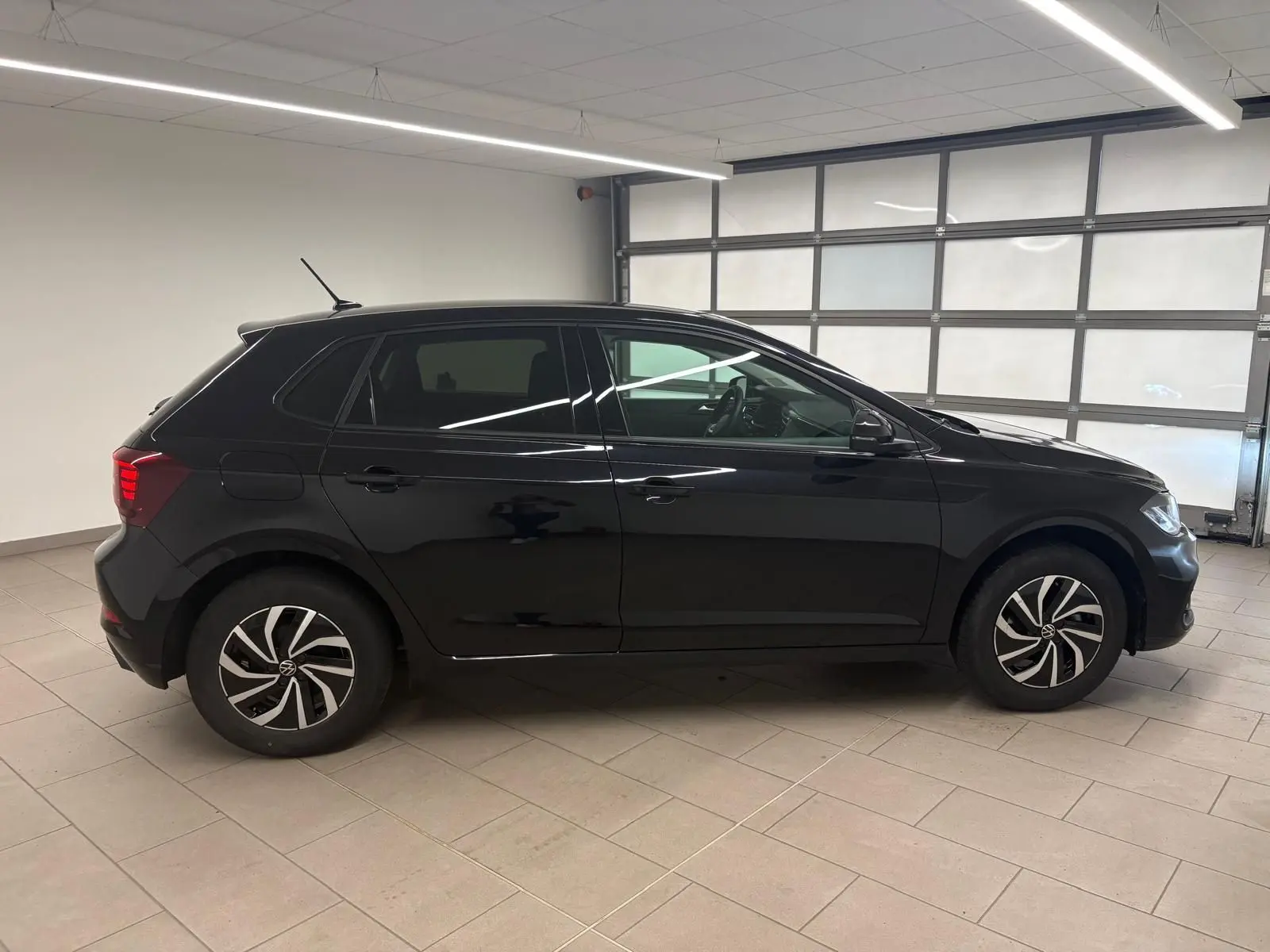 Vue de profil côté gauche d'une Volkswagen Polo noire intense 2025 avec jantes alliage 15 pouces dans un garage.