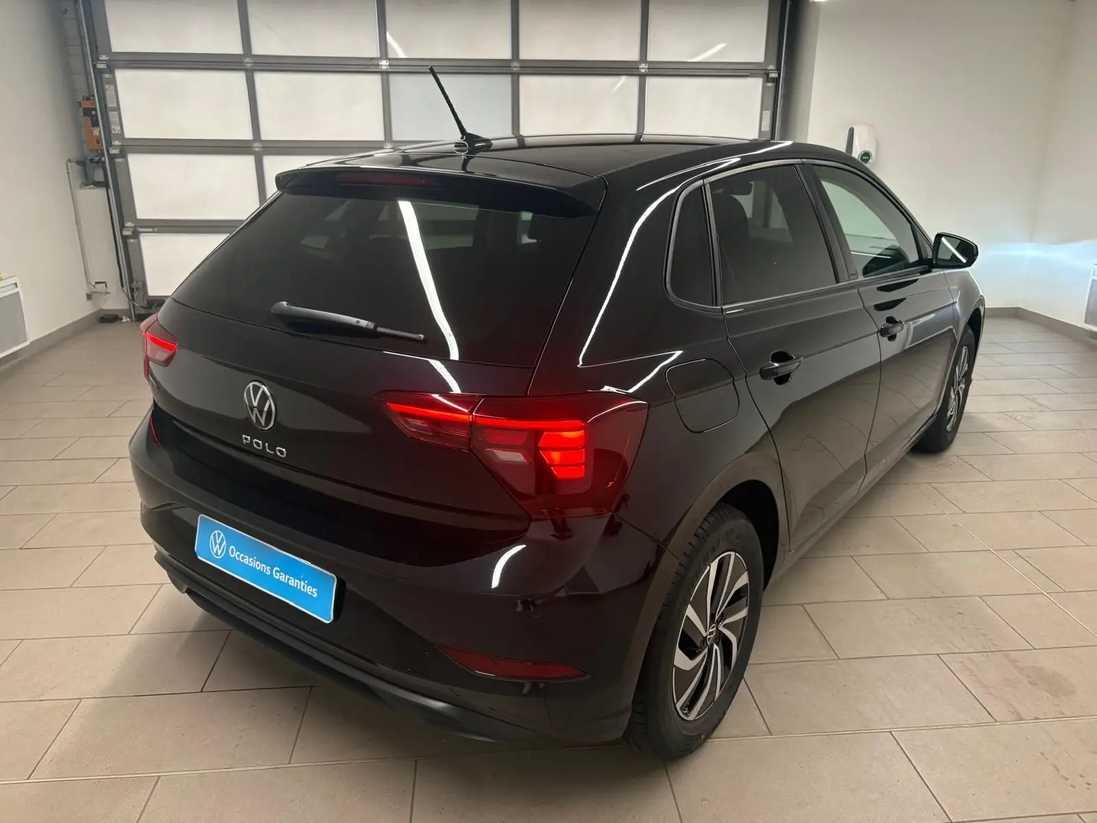 Vue 3/4 arrière droite d'une Volkswagen Polo noire intense avec feux arrière LED et jantes alliage 15 pouces dans un garage.