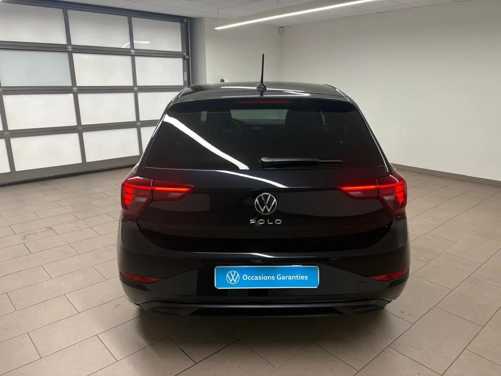Vue arrière d'une Volkswagen Polo noire intense avec feux arrière LED allumés dans un garage lumineux.