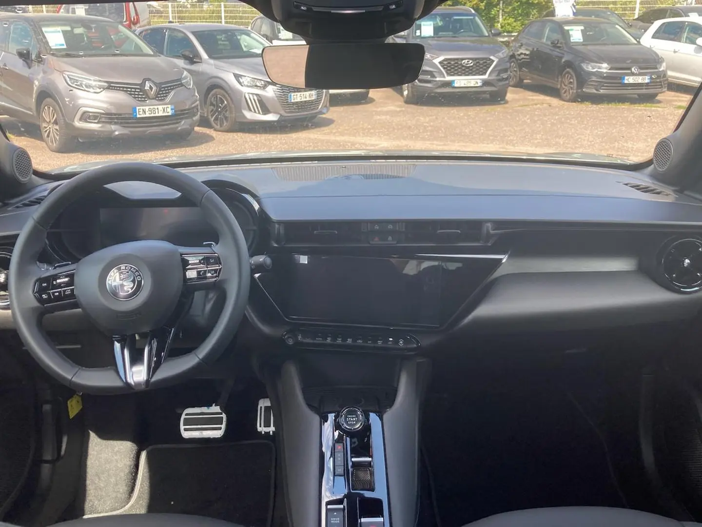 Vue intérieure de l'Alfa Romeo Junior 1.2 hybride 2026, tableau de bord noir avec écran tactile et volant multifonction.