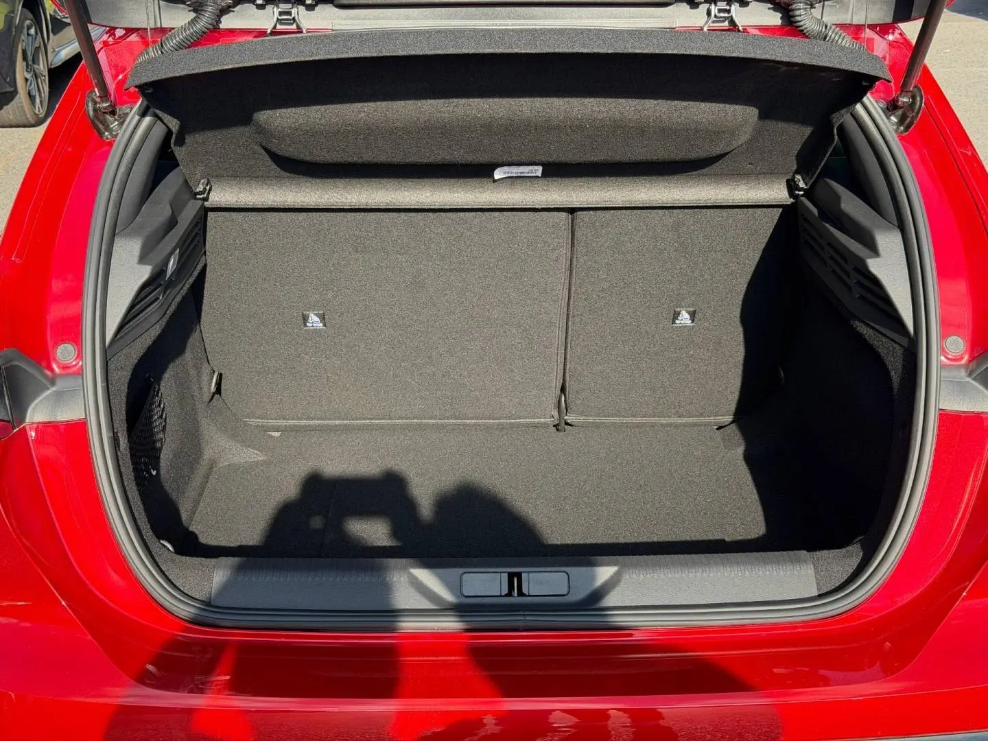 Coffre ouvert vu de l'arrière d'une Peugeot 308 rouge Elixir, montrant un espace de rangement propre et vide.