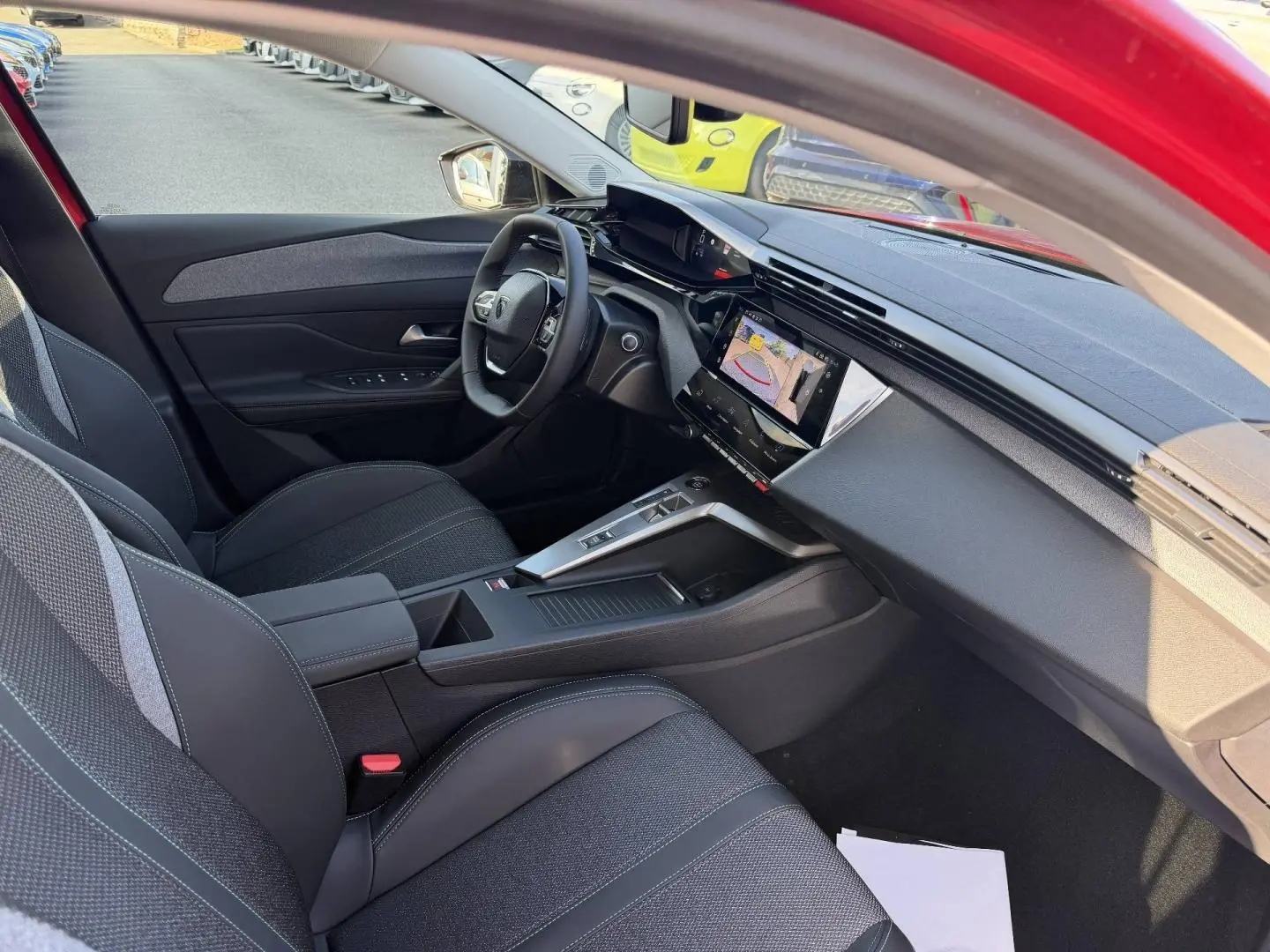 Intérieur côté conducteur de la Peugeot 308 rouge Elixir, avec tableau de bord moderne et écran tactile affichant la caméra de recul.