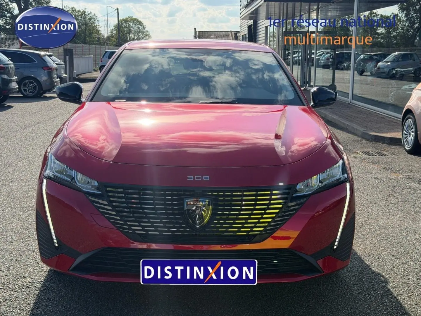 Vue frontale d'une Peugeot 308 rouge Elixir 2025 avec calandre noire et feux LED verticaux allumés.