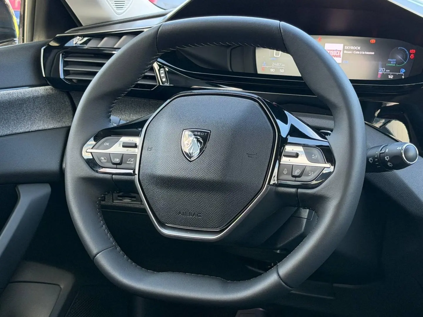 Vue rapprochée du volant multifonction noir de la Peugeot 308 1.2 Hybrid 145ch Allure 2025 avec tableau de bord numérique.