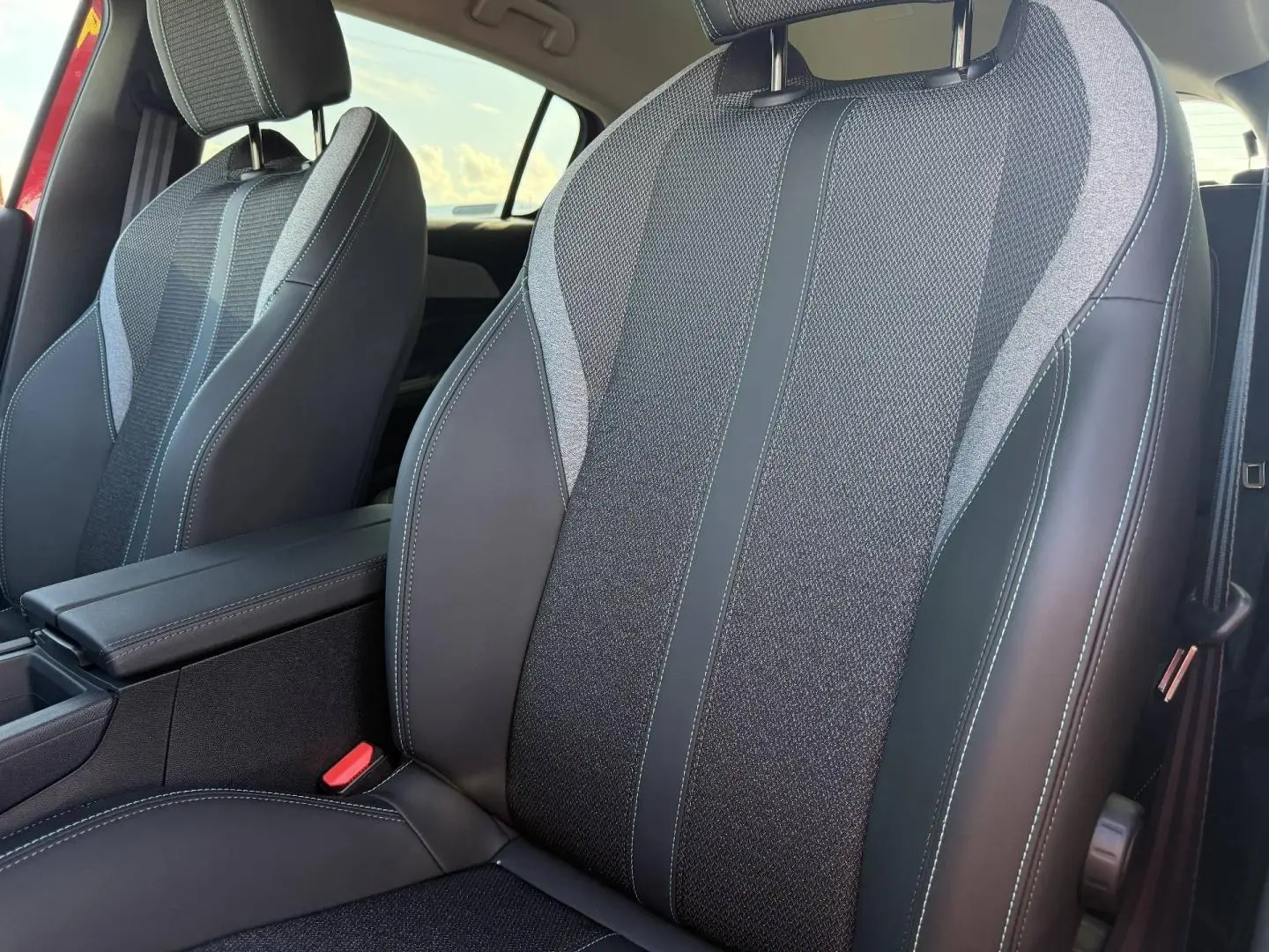 Gros plan sur les sièges avant en tissu et cuir noir avec surpiqûres blanches dans l'habitacle d'une Peugeot 308 rouge.