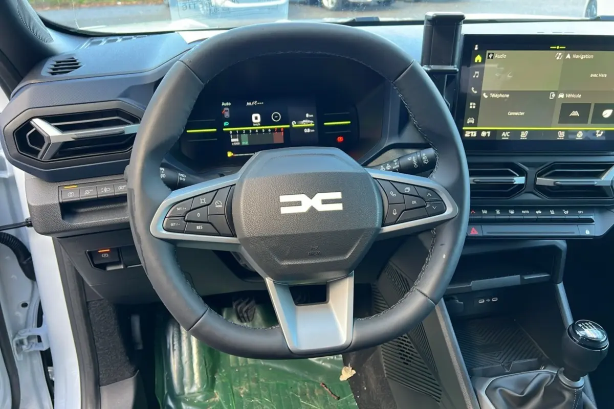 Vue intérieure centrée sur le volant multifonction et le tableau de bord numérique du Dacia Duster blanc glacier 2025.