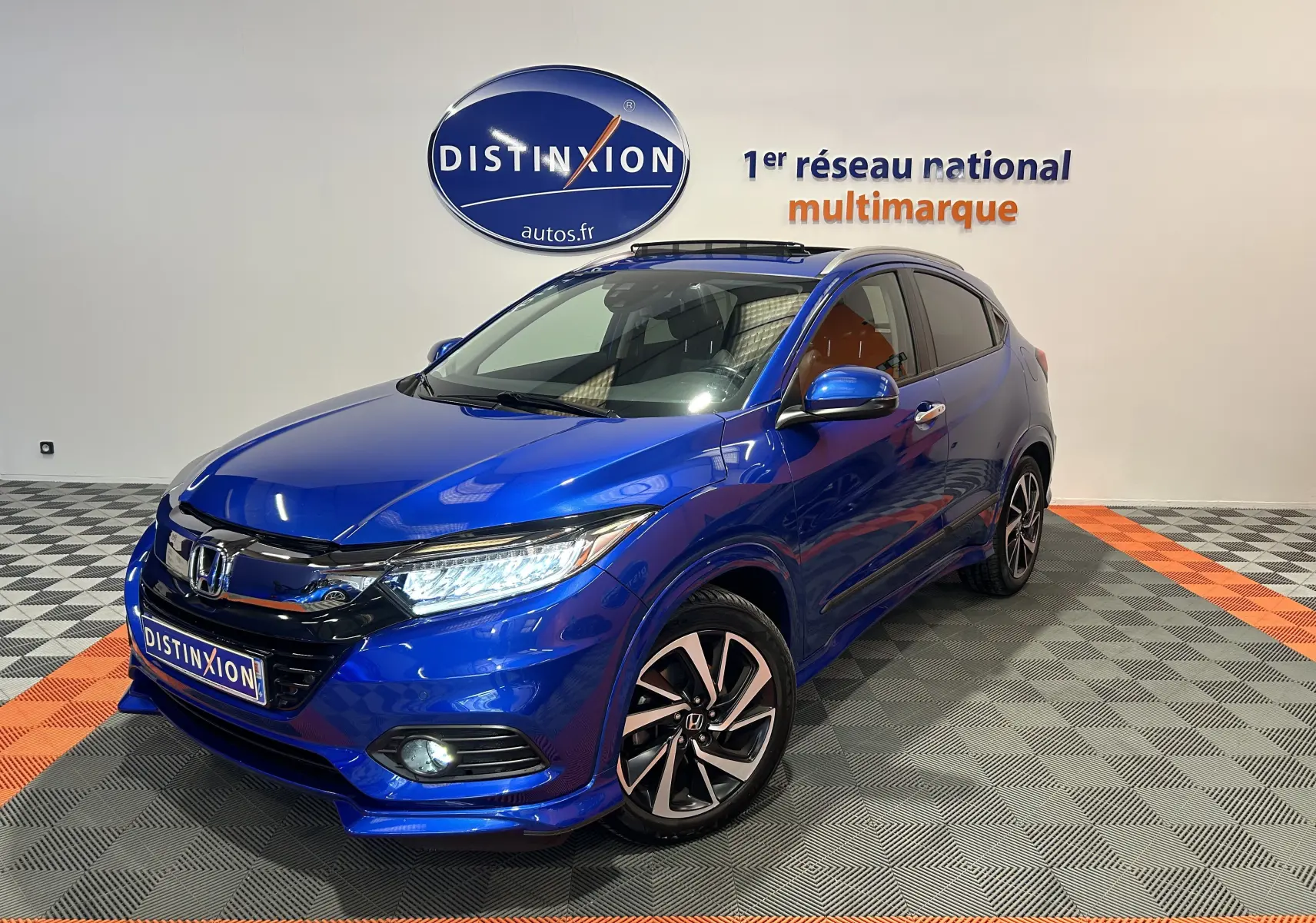 Vue 3/4 avant d'un Honda HR-V bleu avec toit ouvrant, jantes alliage et calandre noire brillante.