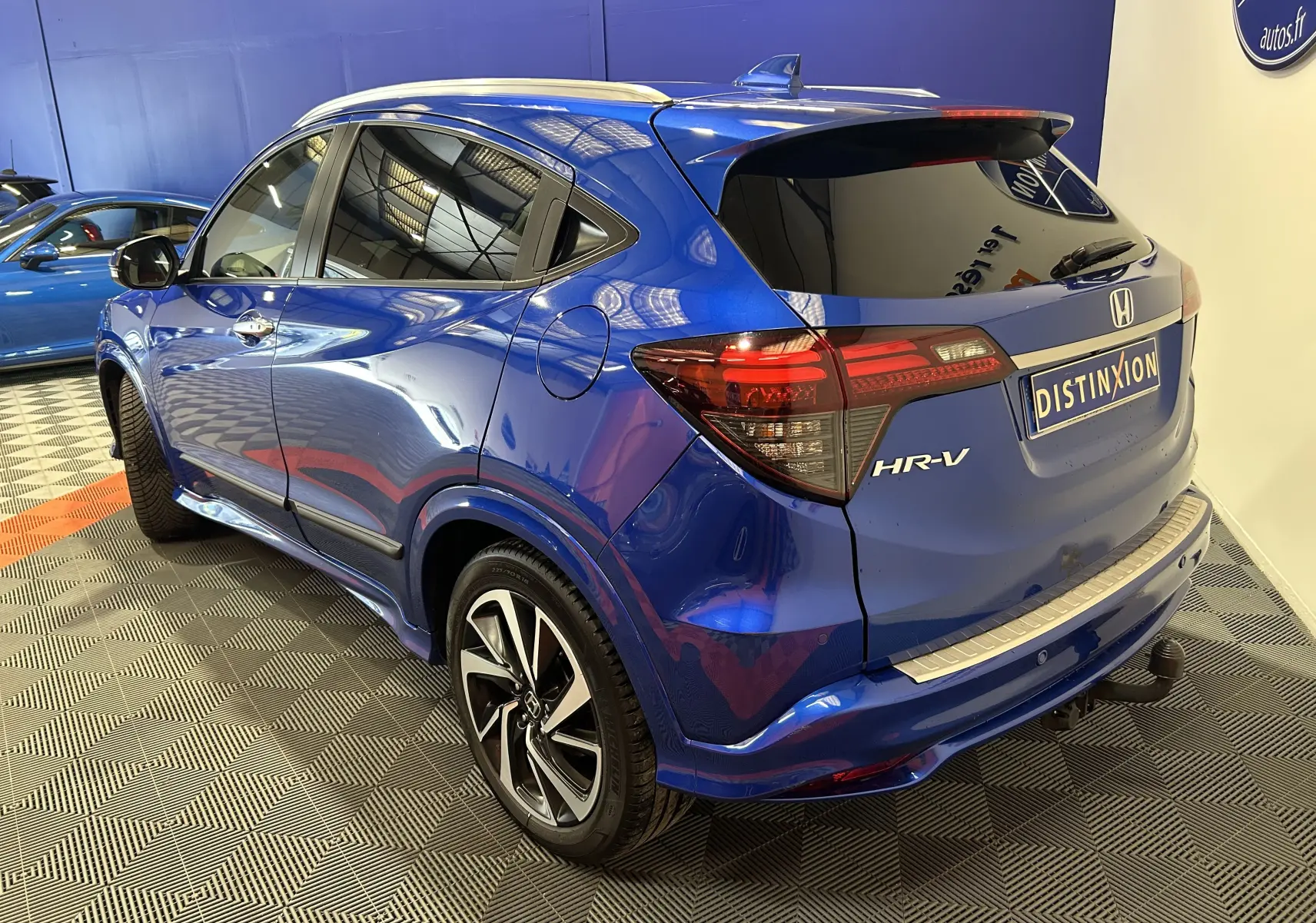 Vue 3/4 arrière droite d'un Honda HR-V bleu avec toit ouvrant et attelage, stationné en intérieur.