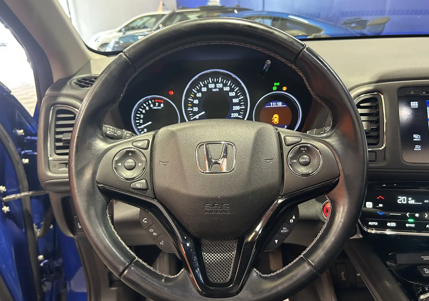 Vue intérieure centrée sur le volant cuir noir du Honda HR-V bleu, avec tableau de bord et commandes visibles.
