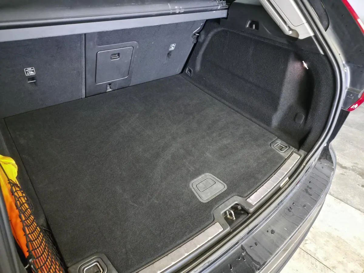 Vue intérieure du coffre ouvert du Volvo XC60 noir, montrant le tapis noir et les fixations latérales.