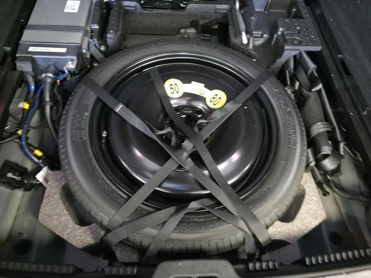 Gros plan sur la roue de secours temporaire noire fixée dans le coffre du Volvo XC60 Ultimate Style Dark 2023.