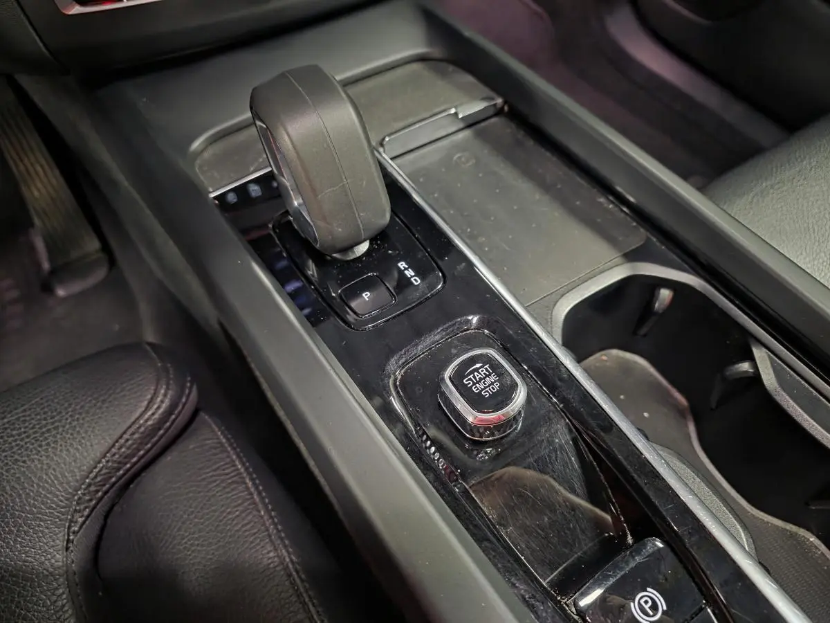 Gros plan sur la console centrale noire du Volvo XC60 2023, avec levier de vitesse et bouton Start/Stop.