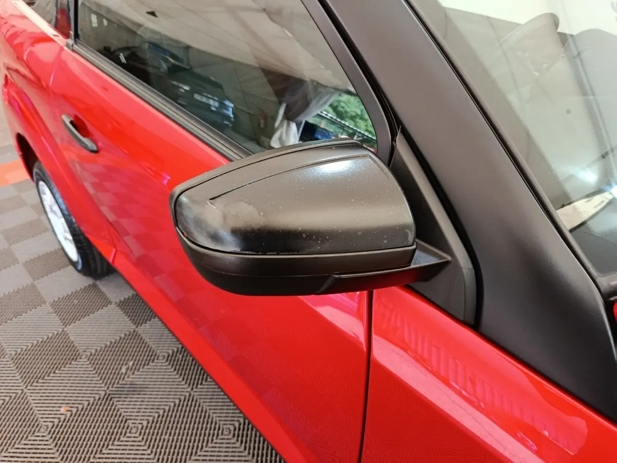 Vue rapprochée du rétroviseur extérieur côté conducteur d'une Aixam Ambition 2024 rouge, avec porte et vitre partiellement visibles.