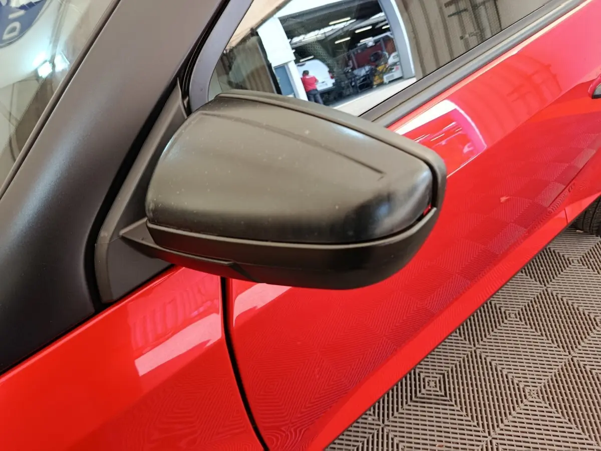 Gros plan sur le rétroviseur extérieur côté conducteur d'une Aixam Ambition 2024 rouge, avec portière visible en arrière-plan.