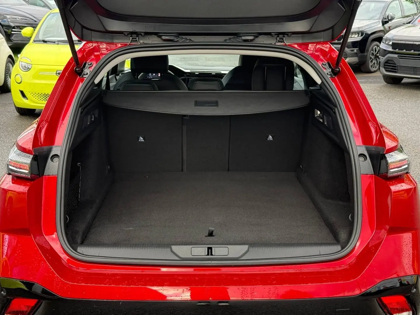 Coffre ouvert vu de l'arrière d'une Peugeot 308 SW rouge Elixir avec banquette arrière et cache-bagages visibles.