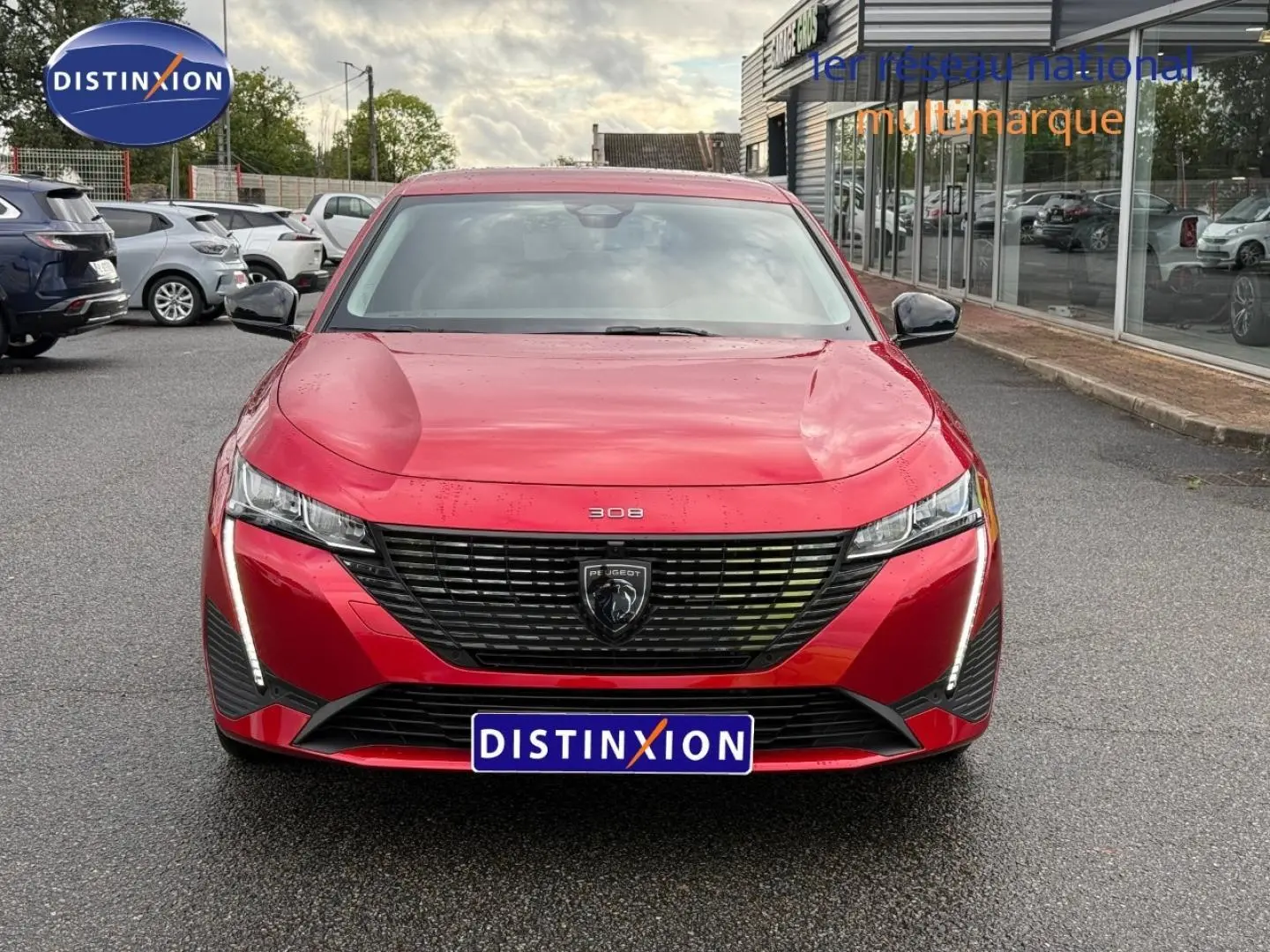Vue avant frontale d'une Peugeot 308 SW rouge Elixir avec calandre noire et feux LED verticaux allumés.