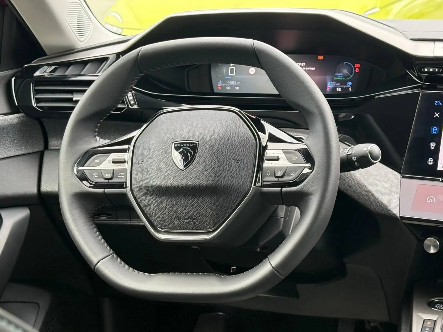 Vue rapprochée du volant multifonction noir de la Peugeot 308 SW 1.2 Hybrid avec tableau de bord numérique en arrière-plan.