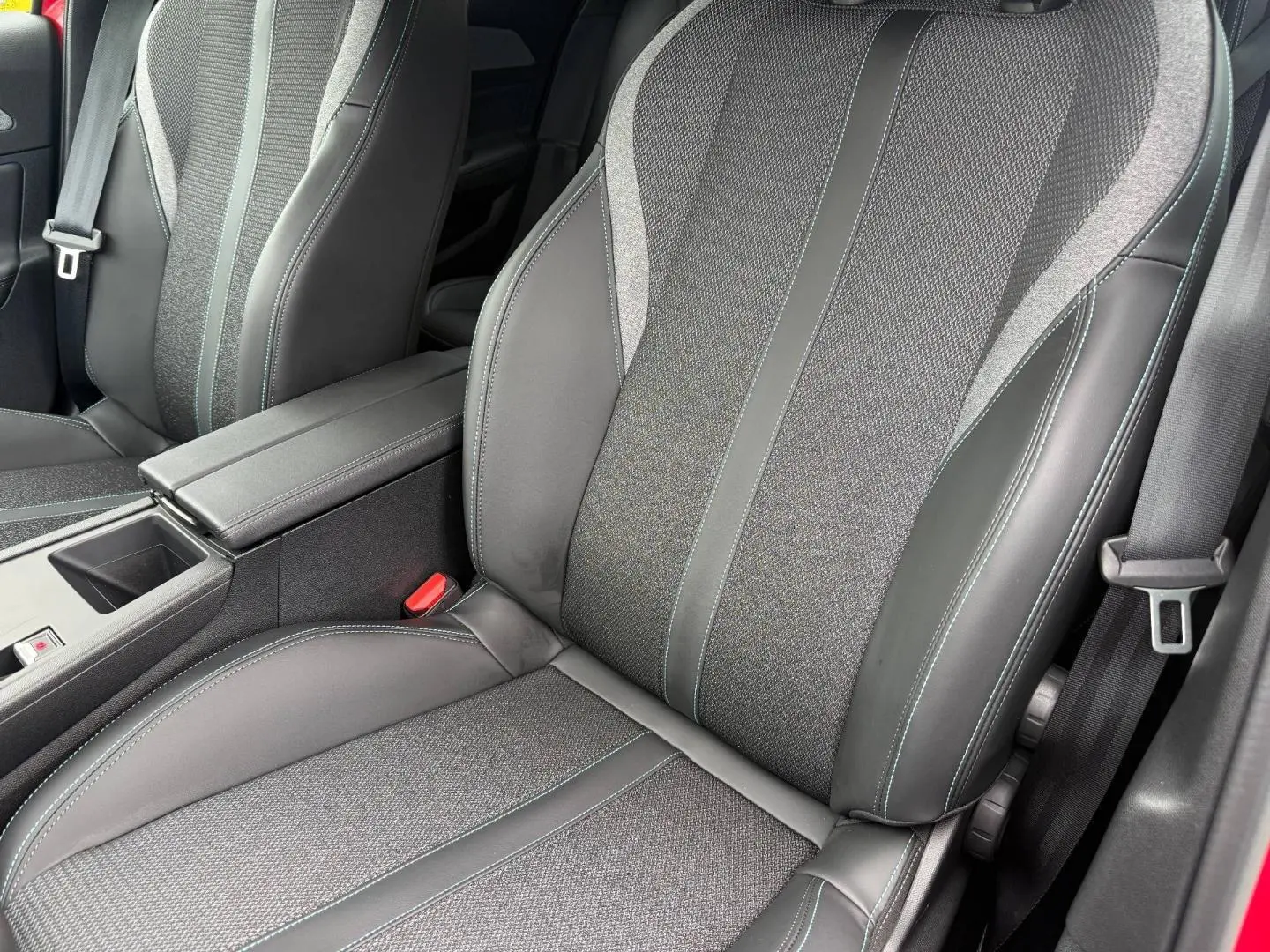 Gros plan sur les sièges avant en tissu et cuir gris avec surpiqûres bleues dans l’habitacle d’une Peugeot 308 SW rouge.