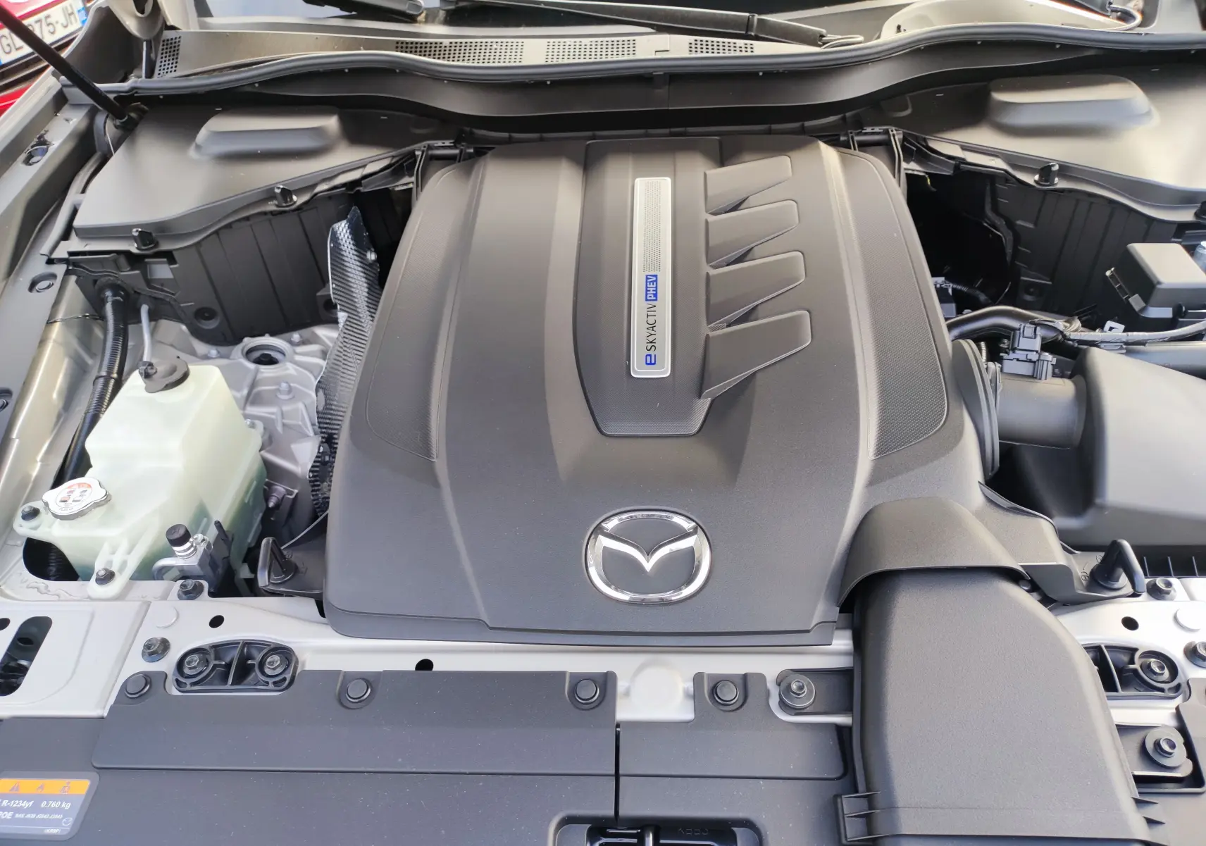 Vue rapprochée du moteur hybride rechargeable du Mazda CX-60 blanc métal avec logo Mazda et inscription Skyactiv PHEV.